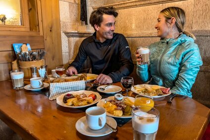 Ein Pärchen sitzt beim Bergfrühstück bei gedecktem Tisch in einer Berghütte. | © Vanessa Strauch - Silvretta Montafon