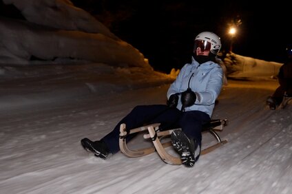 Eine junge Frau fährt auf einem Rodel auf einer Rodestrecke am Abend. | © Silvretta Montafon - Niklas Kirchler
