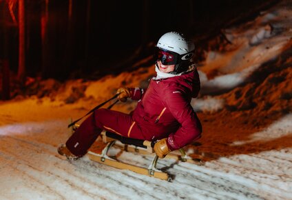 Eine Frau rodelt auf einem Schlitten und lacht. | © Silvretta Montafon - Marie Schilcher