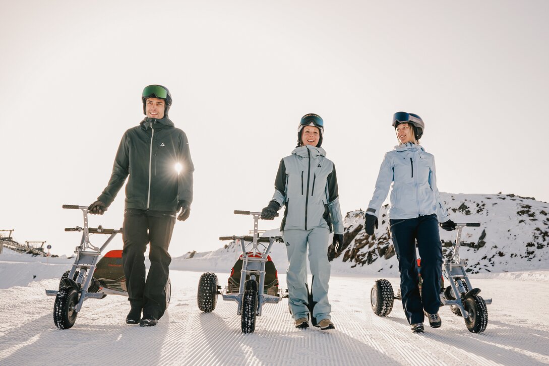 Drei Personen laufen mit einem Mountaincart auf einer Skipiste am Morgen bei Sonnenaufgang. | © Silvretta Montafon - Niklas Kirchler