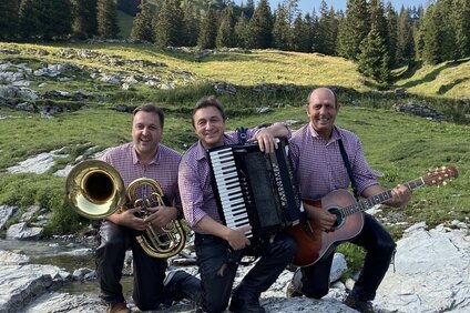 Drei Männer in karierten Hemder mit Musikinstrumenten in den Bergen | © Silvretta Montafon - Werner Konzett