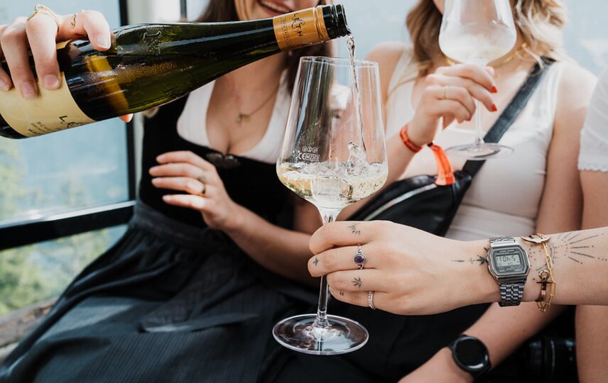 Eine junge Frau schenkt Wein in ein Weinglas in einer Gondel ein | © Silvretta Montafon - GOODGUYPAEZ
