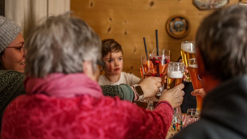 Eine Gruppe von Personen sitzt in einer gemütlichen Berghütte und stoßt mit den Getränken an. | © Vanessa Strauch - Silvretta Montafon