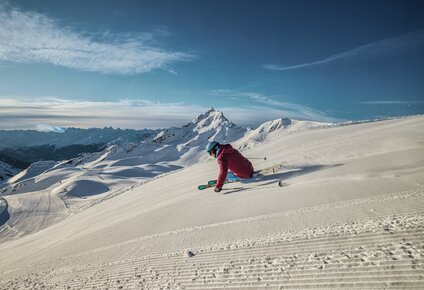 Ein Skifahrer fährt am Morgen über die frisch präparierte Piste mit der Zamangspitze im Hintergrund. | © Silvretta Montafon - Stefan Kothner